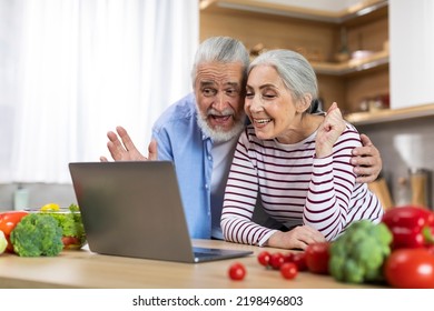 Happy Senior Couple Making Video Call With Laptop While Relaxing In Kitchen, Cheerful Elderly Spouses Waving Hand At Web Camera While Talking To Family, Enjoying Online Communication, Free Space