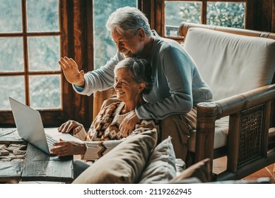 Happy senior couple man and woman doing video call with laptop at home sitting on the floor and chair together having un. Hallo gesture and modern mature people with connection technology leisure - Powered by Shutterstock