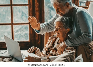 Happy senior couple man and woman doing video call with laptop at home sitting on the floor and chair together having un. Hallo gesture and modern mature people with connection technology leisure - Powered by Shutterstock