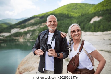 Happy Senior Couple On Hiking Trip On Summer Holiday, Using Binoculars.
