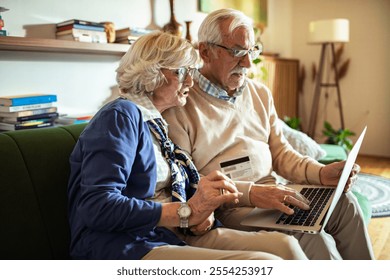 Happy senior couple online shopping with laptop on couch at home - Powered by Shutterstock