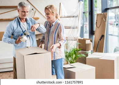 Happy Senior Couple Packing Cardboard Boxes During Relocation 