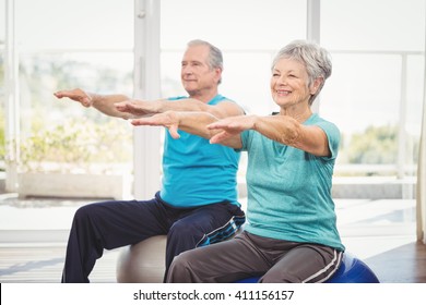 Happy senior couple performing exercise while sitting on exercise ball at home - Powered by Shutterstock