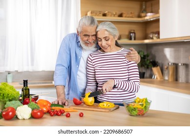 Happy Senior Couple Preparing Healthy Salad Together In Kitchen Interior, Smiling Elderly Husband And Wife Cooking Vegetarian Lunch Or Dinner At Home, Woman Chopping Vegetables, Copy Space