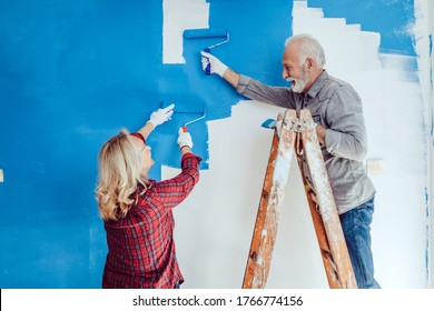 Happy senior couple renovating their home. They are painting a wall together. - Powered by Shutterstock