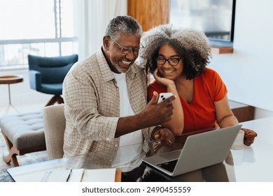 Happy senior couple reviewing budget on smartphone and laptop, showcasing technology use in financial management at home. - Powered by Shutterstock