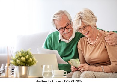 Happy Senior Couple Reviewing Domestic Finances Together. Smiling Old Woman Entering Payment Data Into Banking Application On Computer While Pleasant Mature Husband Reading Paper Tax Document.