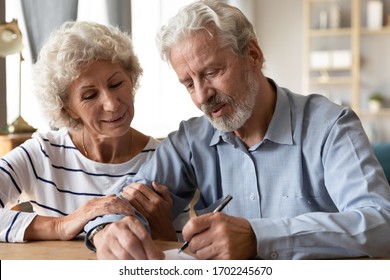 Happy senior couple signing legal documents, making purchasing deal, smiling mature wife and husband buying house or taking loan, satisfied senior man putting signature on insurance contract