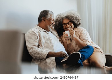 Happy senior couple sitting comfortably and enjoying coffee at home, sharing a joyful moment filled with love and laughter. - Powered by Shutterstock