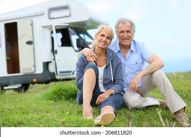 Happy senior couple sitting in grass, camper in background