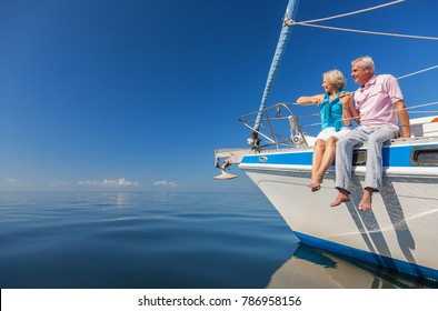 A happy senior couple sitting on the side of a sail boat on a calm blue sea