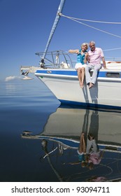 A Happy Senior Couple Sitting On The Front Of A Sail Boat On A Calm Blue Sea