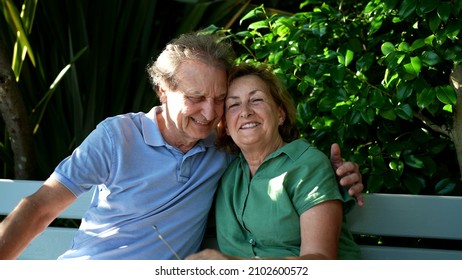 Happy Senior Couple Sitting Outside At Park Bench