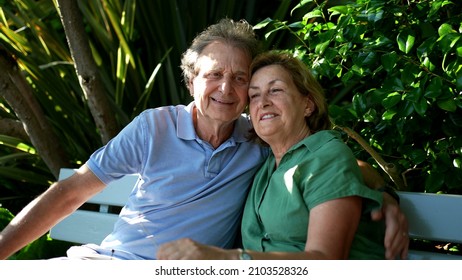 Happy Senior Couple Sitting Outside At Park Bench