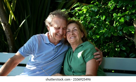 Happy Senior Couple Sitting Outside At Park Bench