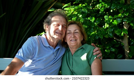 Happy Senior Couple Sitting Outside At Park Bench