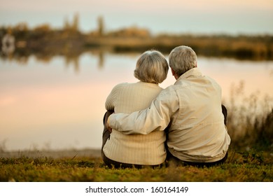 Feliz pareja senior sentada en verano cerca del lago durante el atardecer