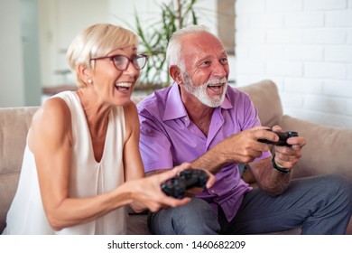 Happy Senior Couple Sitting Together In Their Living Room And Laughing While Playing A Video Game.