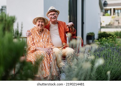 Happy senior couple sitting together in garden bench, smiling and looking at camera. - Powered by Shutterstock