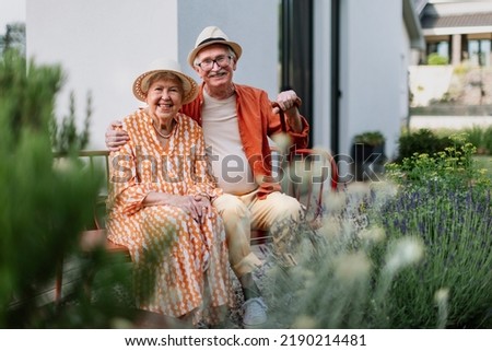 Happy senior couple sitting together in garden bench, smiling and looking at camera.