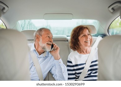 Happy Senior Couple With Smartphone Sitting In Car, Talking.