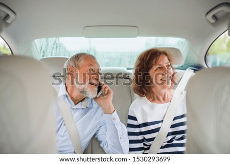 Happy senior couple with smartphone sitting in car, talking.