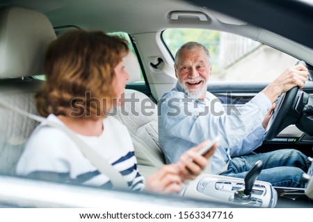 Happy senior couple with smartphone sitting in car, going on trip.