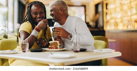 Happy senior couple smiling cheerfully while eating together in a coffee shop. Carefree senior couple having a good time in a restaurant. Mature couple enjoying their retirement together. - Powered by Shutterstock