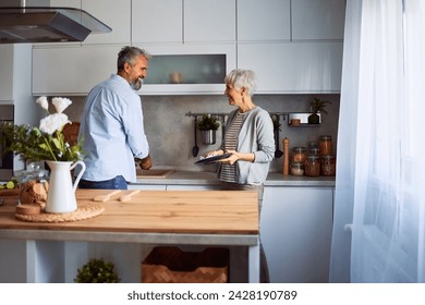 A happy senior couple smiling at each other while washing and cleaning the dishes together and standing in the kitchen. - Powered by Shutterstock