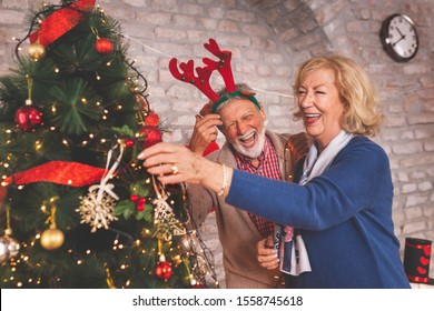 Happy senior couple standing next to a nicely decorated Christmas tree, decorating it and having fun at home on Christmas day - Powered by Shutterstock