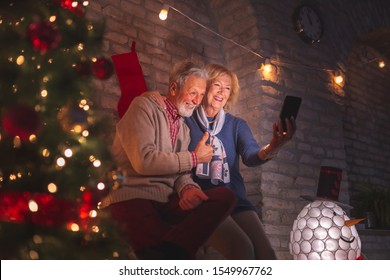 Happy senior couple taking a selfie next to a nicely decorated Christmas tree, having fun at home while celebrating Christmas Eve - Powered by Shutterstock