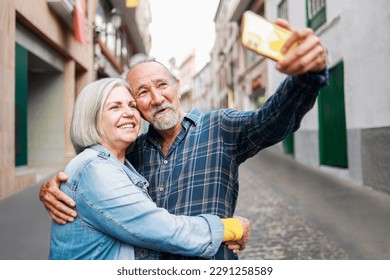 Happy senior couple taking selfie with mobile phone outdoor - Elderly tourist and travel vacations - Focus on faces - Powered by Shutterstock