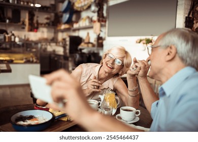 Happy senior couple taking selfie while eating at cozy bistro - Powered by Shutterstock