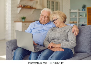 Happy Senior Couple Talking To Children And Grandchildren Via Video Chat Sitting On Sofa With Laptop. Grandparents Staying At Home, Using Modern Computer, Video Calling Family Or Shopping Online