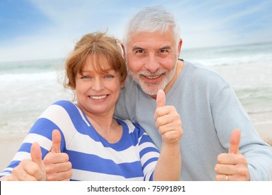 Happy senior couple with thumbs up at the beach