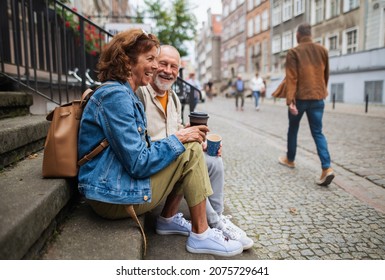 Happy senior couple tourists sitting on stairs and having take away coffee outdoors in town - Powered by Shutterstock