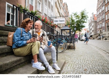 Happy senior couple tourists sitting on stairs and having take away coffee outdoors in town ストックフォト © 