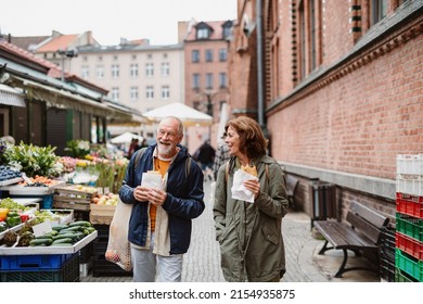 Happy senior couple tourists with snack in town on outdoor market. - Powered by Shutterstock