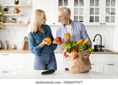 Happy Senior Couple Unpacking Paper Bag With Fresh Organic Vegetables And Fruits After Grocery Shopping, Cheerful Elderly Spouses Standing In Cozy Kitchen Interior At Home, Copy Space - Powered by Shutterstock