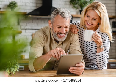 Happy senior couple using digital tablet in kitchen at home - Powered by Shutterstock