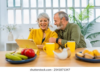 Happy senior couple using digital tablet at home while eating healthy breakfast - Powered by Shutterstock