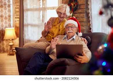 Happy Senior Couple Using Laptop And Greeting Someone During Video Call On Christmas.