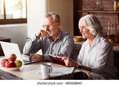 Happy senior couple using laptop at the kitchen - Powered by Shutterstock