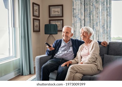 Happy senior couple using remote control to change channel. Seniors watch TV for entertainment while man using remote control. Wife and old man sitting on couch in living room with television show. - Powered by Shutterstock