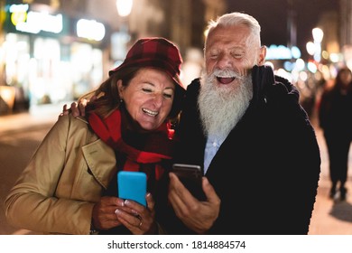 Happy senior couple using smart phones in city street at night time - Focus on hipster man face - - Powered by Shutterstock