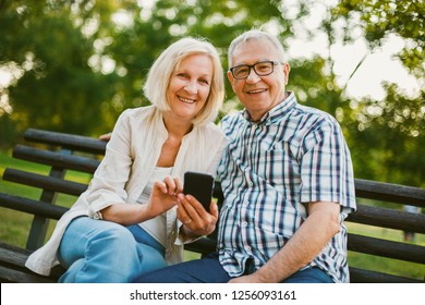 Happy senior couple is using smartphone in park. - Powered by Shutterstock