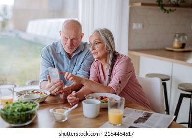 Happy senior couple using smartphone during eating dinner together at home. - Shutterstock ID 2164464517