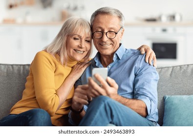 Happy Senior Couple Using Smartphone Browsing Internet Together Sitting On Couch At Home And Hugging. Cellphone Users Use Mobile Application. Older Spouses Texting On Phone. Communication Concept - Powered by Shutterstock