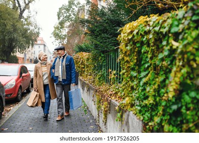 Happy senior couple walking outdoors on street in city, carrying shopping bags. - Powered by Shutterstock