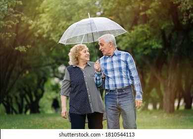 Happy senior couple walking in park during rain under umbrella - Powered by Shutterstock